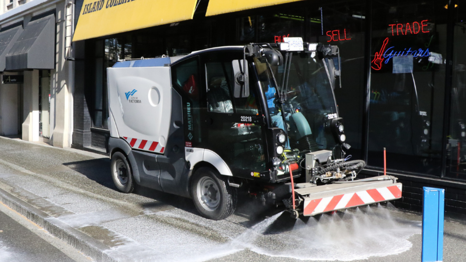 Image of a sidewalk cleaning machine cleaning a downtown sidewalk. 