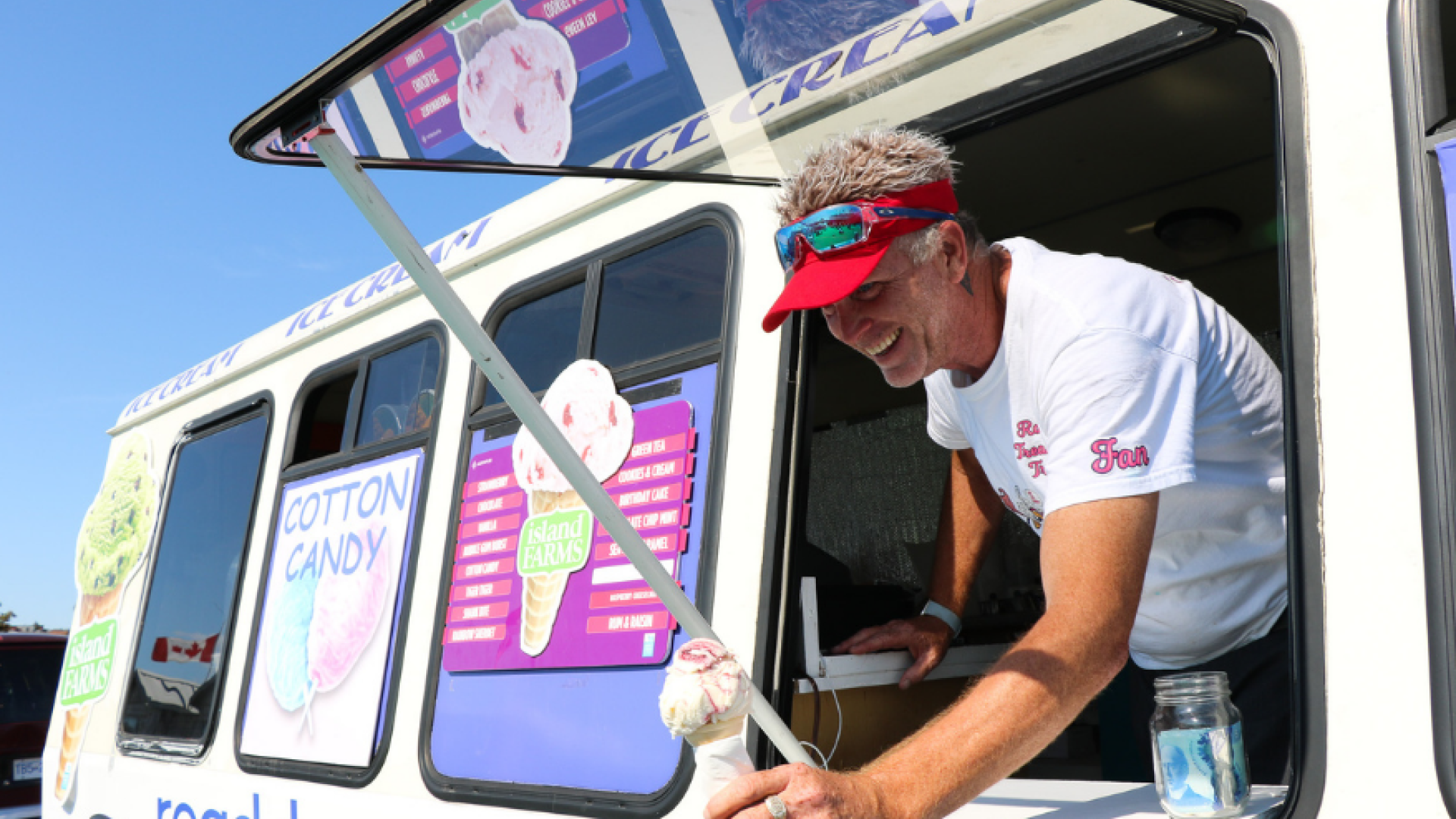 Image of an ice cream food truck with vendor leaning out of window handing an ice cream cone to someone not in view.