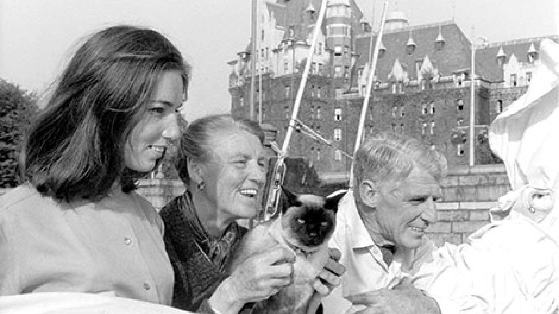 An archival image in black and white of three people laughing in the foreground with the Empress Hotel in the background