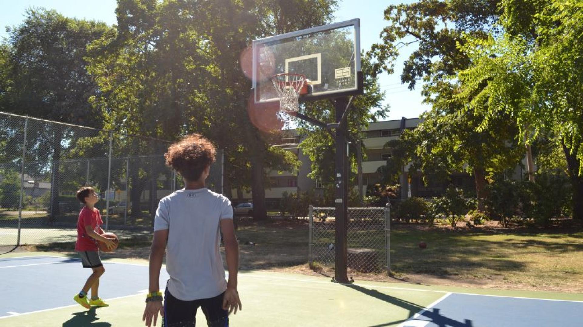 two kids playing basketball at an outdoor court