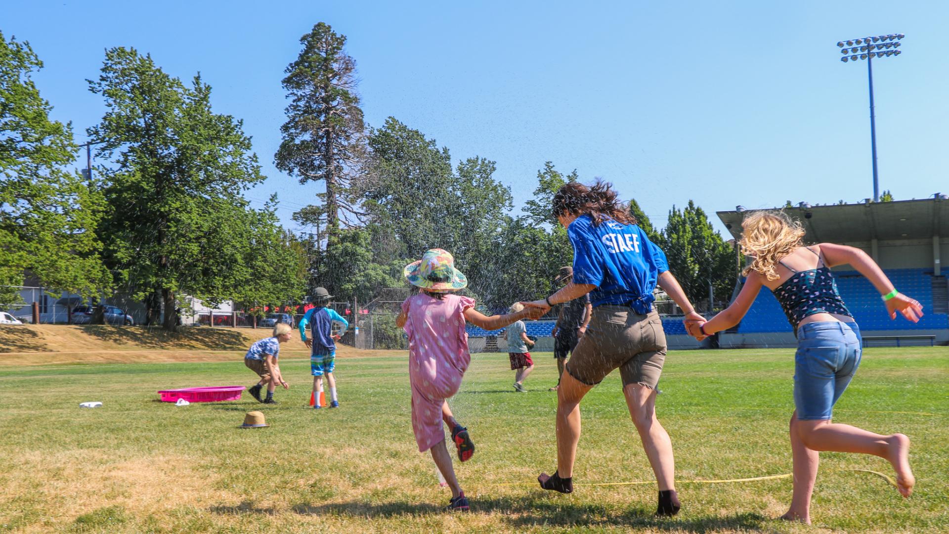 summer camp staff and kids run through sprinkler
