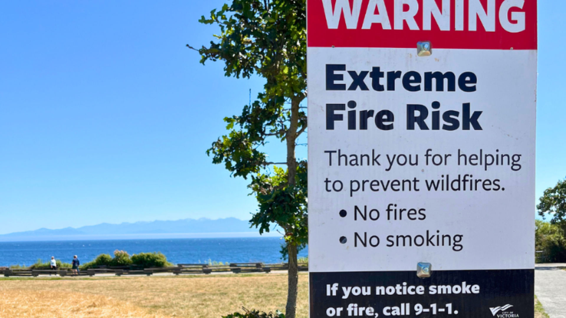 Extreme fire risk sign posted along Dallas Road, with grass and ocean in the background.