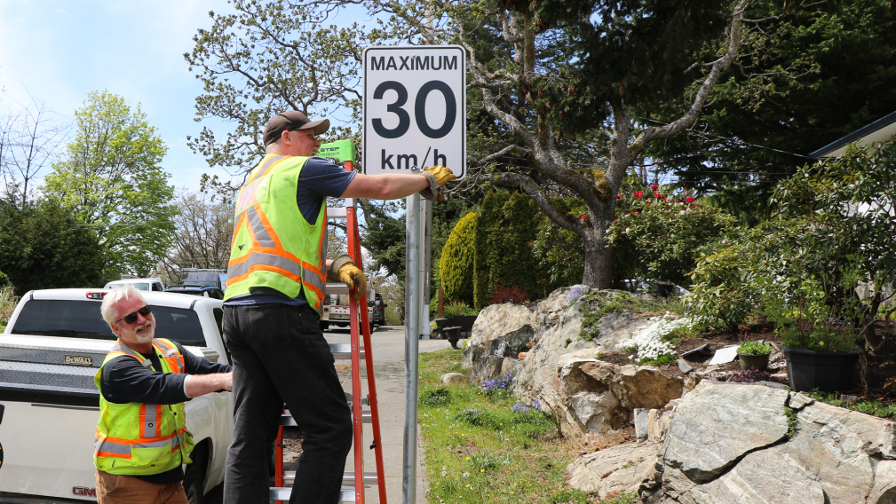 An image of two City workers installing a new 30 km speed limit sign