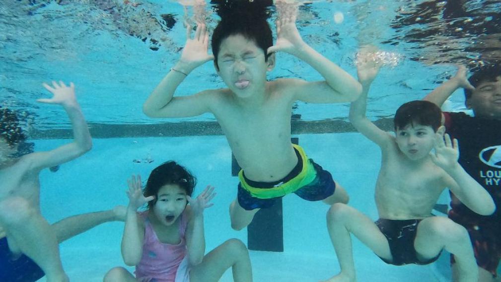 A group of kids makes faces underwater at the pool