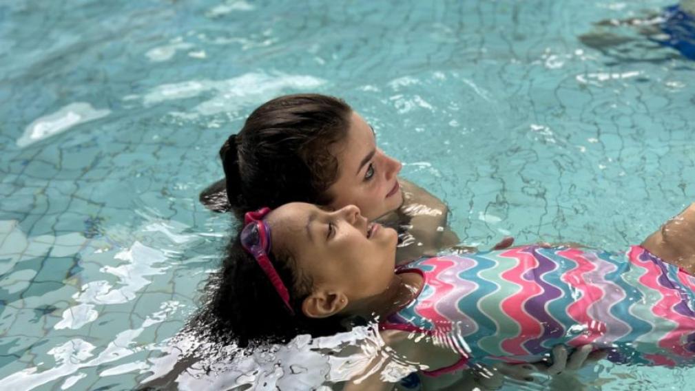 A swim instructor helps a child float in the pool