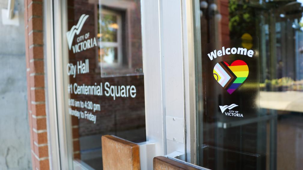 An image of the door to City Hall with a sticker saying the word "welcome" with a rainbow decal