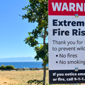 Extreme fire risk sign posted along Dallas Road, with grass and ocean in the background.